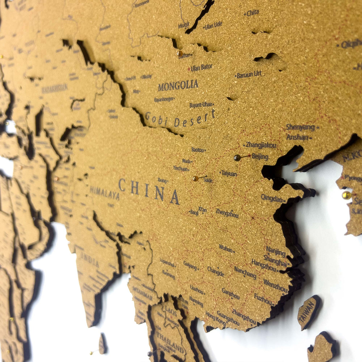 Layered laser-cut cork world map with dark brown edges and labeled continents