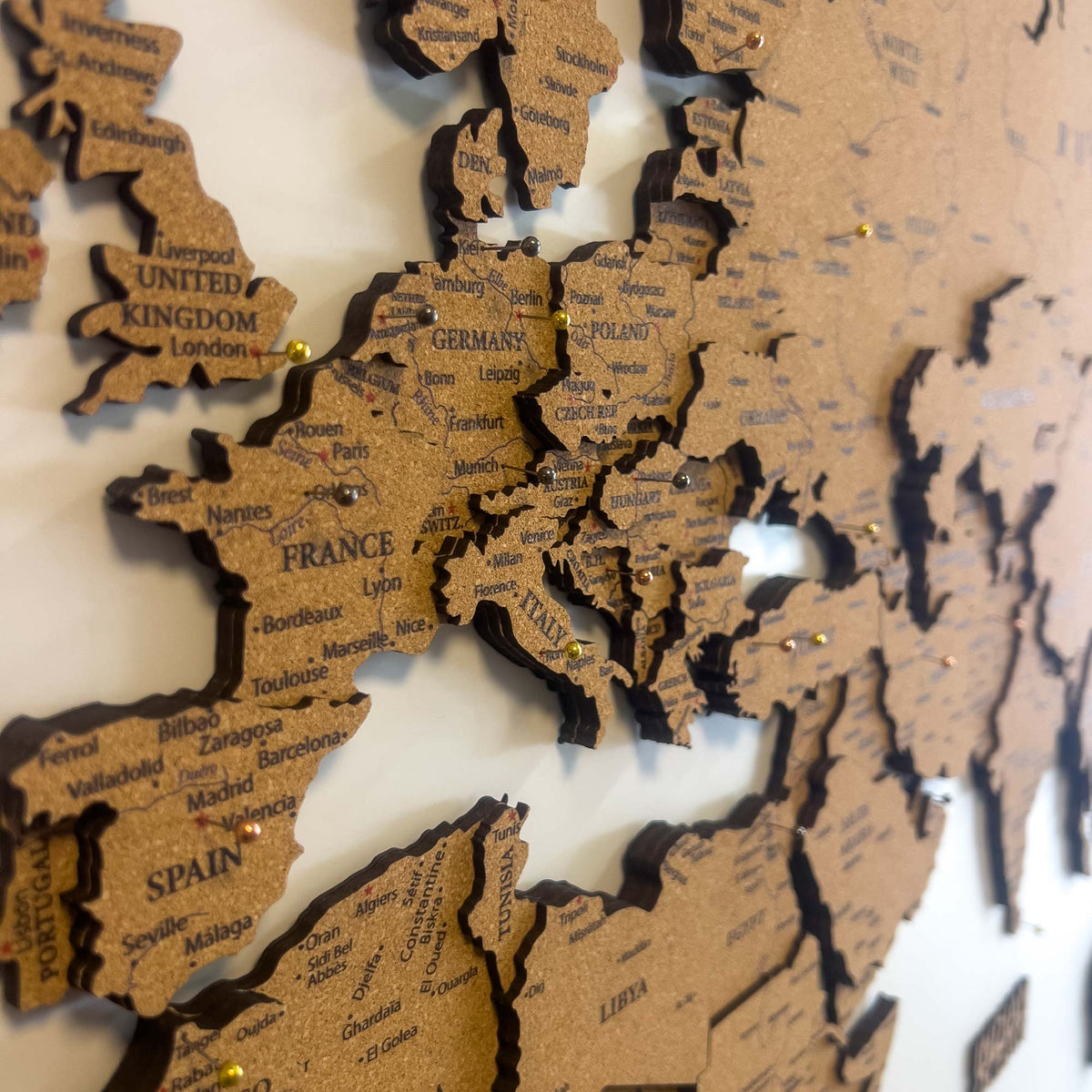 Layered laser-cut cork world map with dark brown edges and labeled continents